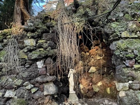 Aus Bruchsteinen aufgeschichtete Grotte im Park der Villa Haas mit einer kleinen Figur in der Nische, darüber der Glockenturm der Villa