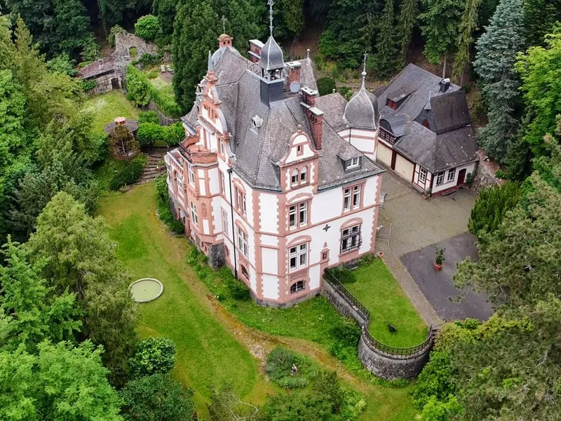 Luftaufnahme der Villa Haas von oben, unterhalb des Hauses die abfallende Parkwiese mit dem Gartenteich, ringsum bewaldete Hänge