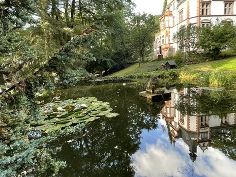 Gartenteich im Park der Villa Haas mit Seerosen, im Wasser spiegelt sich die historistische Villa mit ihrem Turm
