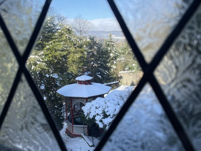 Blick durch eine Butzenscheibe auf das schneebedeckte Teehaus im Park der Villa Haas