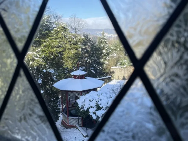 Blick durch eine Butzenscheibe auf das schneebedeckte Teehaus im Park der Villa Haas