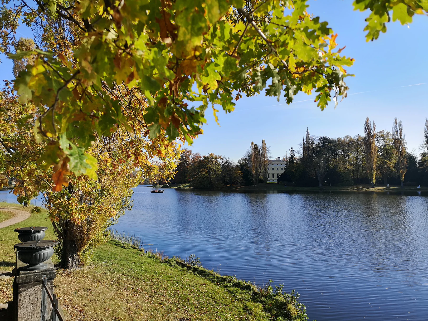 Blick über den Wörlitzer See auf das klassizistische Schloss Wörlitz im herbstlichen Landschaftsgarten, mit einer Gondel auf dem Wasser