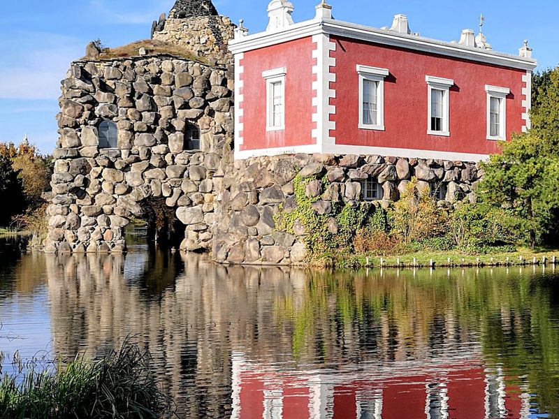 Villa Hamilton auf der Insel Stein, ein rotes klassizistisches Gebäude auf einem künstlichen Felsen, gespiegelt im See