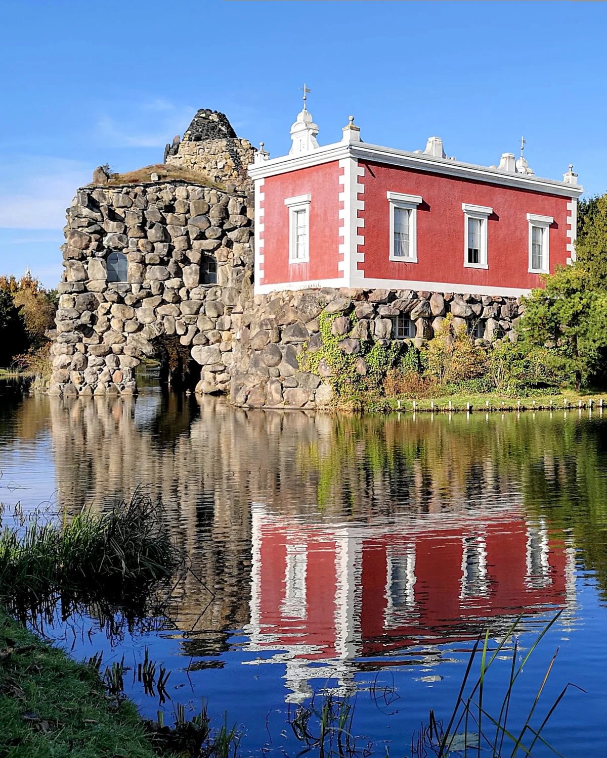 Villa Hamilton auf der Insel Stein im Wörlitzer Park, ein rotes klassizistisches Gebäude auf einem künstlichen Felsen, gespiegelt im See